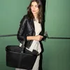 A woman walks with a black mesh basket in front of a green wall. Voir les images du produit