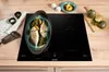 A Gorenje induction hob with a pot of fish and vegetables cooking on it, placed on a wooden countertop. Voir les images du produit