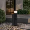A modern outdoor lamp post with integrated electrical outlets and a motion sensor, situated on a stone patio next to a building. Produktbild-Vorschau
