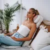 A woman is relaxing on a bed with a massage device on her neck. Produktbild-Vorschau