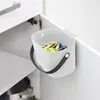 A gray compost bin with a black handle is hanging on the inside of a white cabinet door, filled with batteries. Voir les images du produit