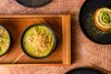 A top-down view of a minimalist table setting with green soup and a dessert. Náhľad obrázku produktu