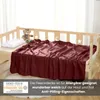 A burgundy fleece blanket is draped over a wooden crib, with a teddy bear and a pillow on the crib. Náhľad obrázku produktu