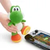A knitted Yoshi toy is held by hands next to a Nintendo Wii U gamepad. Produktbild-Vorschau