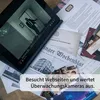 A tablet displaying a security camera feed is placed on a table with various documents and photographs, suggesting a mystery or investigation theme. Produktbild-Vorschau