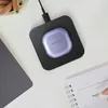 A purple Samsung wireless earbud case is charging on a black wireless charging pad, placed on a white desk next to a notebook and a laptop. Produktbild-Vorschau