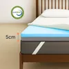 A close-up view of a mattress topper with multiple layers, placed on a bed frame. A pillow is visible on top of the topper. Náhled obrázku produktu