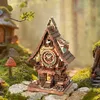 A detailed 3D wooden puzzle of a cuckoo clock, set in a whimsical forest scene with miniature houses and mushrooms. Náhľad obrázku produktu