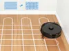 A black robot vacuum cleaner is shown on a wooden floor, demonstrating its cleaning path with white lines and arrows, and also picking up debris. Two diagrams illustrating cleaning patterns are in the upper left corner. Produktbild-Vorschau
