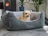 A small dog is resting comfortably in a plush dog bed in a modern living room setting. Produktbild-Vorschau
