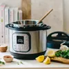 An Instant Pot multi-cooker is shown on a countertop with ingredients like lemons, garlic, and herbs, suggesting it's being used for cooking. Náhled obrázku produktu