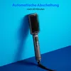 A gray hair straightening brush is shown leaning against a bright blue wall, with a dark blue surface in the foreground. Produktbild-Vorschau