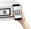 A hand holds a smartphone displaying a QR code, which is being scanned by a printer also displaying a QR code on its screen. Podgląd zdjęcia produktu