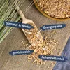 A wooden scoop filled with birdseed, with some spilled onto a burlap surface. There are also some blades of grass in the background. Produktbild-Vorschau