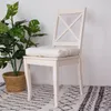 A white chair with a cream cushion sits next to a potted plant on a patterned rug. Produktbild-Vorschau