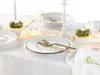 A beautifully set table with white plates and gold cutlery, decorated with small floral arrangements and candles. Náhľad obrázku produktu