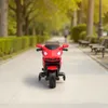 A red toy motorcycle is parked on a paved path in a park with trees and benches in the background. A person is walking in the distance. Produktbild-Vorschau