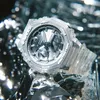 A close-up shot of a transparent G-Shock watch with a metallic dial, set against a textured, reflective background. Produktbild-Vorschau