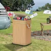 A bamboo trash can filled with bottles and cans is placed on a grassy area near a car and tents, suggesting an outdoor event or camping trip. Produktbild-Vorschau