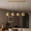 A modern pendant light fixture with four beige lampshades and gold accents hangs from a ceiling in a living room setting. Produktbild-Vorschau