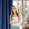 A young woman holding a mug stands by a window with a Christmas tree and snowy scenery outside. Anteprima dell’immagine prodotto