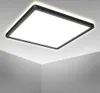 A square LED panel light is mounted on a white ceiling, casting a bright, neutral white light. Voir les images du produit