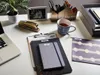 A desk with office supplies including a laptop, stapler, notebooks, a mug, and a filing tray. Produktbild-Vorschau