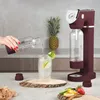 A person is pouring water from a bottle into a glass next to a soda maker. Podgląd zdjęcia produktu