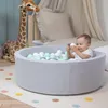 A baby playing in a light gray ball pit filled with colorful balls, with a giraffe plush toy in the background. Produktbild-Vorschau