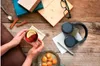 A person's hands holding a cup of tea with lemon, surrounded by books, headphones, cinnamon sticks, and cookies on a wooden table. Voir les images du produit