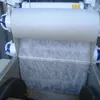 A roll of white filter fleece material is shown, partially unrolled and laid out over a metal trough with black rollers. Produktbild-Vorschau