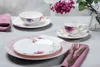 A table setting with floral-patterned dinnerware and a vase of flowers. Produktbild-Vorschau