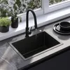 A black kitchen sink with a black faucet is shown with water running into it. There are plants on the windowsill behind the sink and a stack of black plates to the right. Náhled obrázku produktu