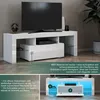 A white high-gloss TV stand with a TV on top, and a media console inside. There are also inset images showing details of the stand. Náhled obrázku produktu