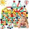 A young girl is lying down and smiling, with a large structure made of colorful magnetic building blocks behind her. There are also smaller magnetic block structures in the foreground. Decorative elements like a sun and clouds are in the background. Voir les images du produit