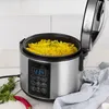 A silver digital rice cooker with its lid open, filled with yellow rice and garnished with parsley, sits on a light wooden surface. Náhľad obrázku produktu