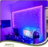 A gaming setup with a desk, monitors, and a textured wall paneling illuminated by LED lights. Podgląd zdjęcia produktu