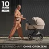 A woman walks a stroller on a sidewalk next to a textured wall. Produktbild-Vorschau