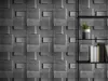 A close-up view of decorative wall panels with a brick-like texture, mounted on a wall. A black shelf unit with a potted plant and books is visible on the right side. Náhled obrázku produktu