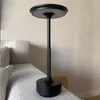 A black LED table lamp is placed on a couch next to a pillow, with a wall in the background. Produktbild-Vorschau