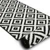 A black and white geometric patterned rug is shown partially rolled up on a white background. Anteprima dell’immagine prodotto