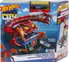 The image shows the packaging of a Hot Wheels City Scorpion Flex Attack playset, featuring a large red scorpion toy attacking a blue building with cars. The packaging includes product branding, a toy car, and descriptive text. Voir les images du produit