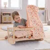 A young girl is playing with a wooden doll's cradle in a room. Produktbild-Vorschau