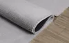 A close-up view of a rolled-up gray rug on a wooden floor. Produktbild-Vorschau