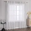 A white sheer curtain with a floral pattern hangs on a window. Produktbild-Vorschau