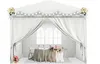A white tent set up for an event, decorated with flowers and lights, with a table and chairs inside. Voir les images du produit