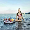 A woman in a swimsuit sits in the ocean next to an inflatable drink tray filled with drinks and fruit. Náhled obrázku produktu