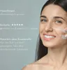 A woman is smiling and applying a product to her face. Produktbild-Vorschau