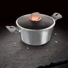 A Berlinger Haus pot with a glass lid and copper accents, placed on a dark, textured surface with a black background. Náhled obrázku produktu