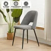 A gray dining chair with black legs is shown in a room with a plant and a window with blinds. Náhled obrázku produktu
